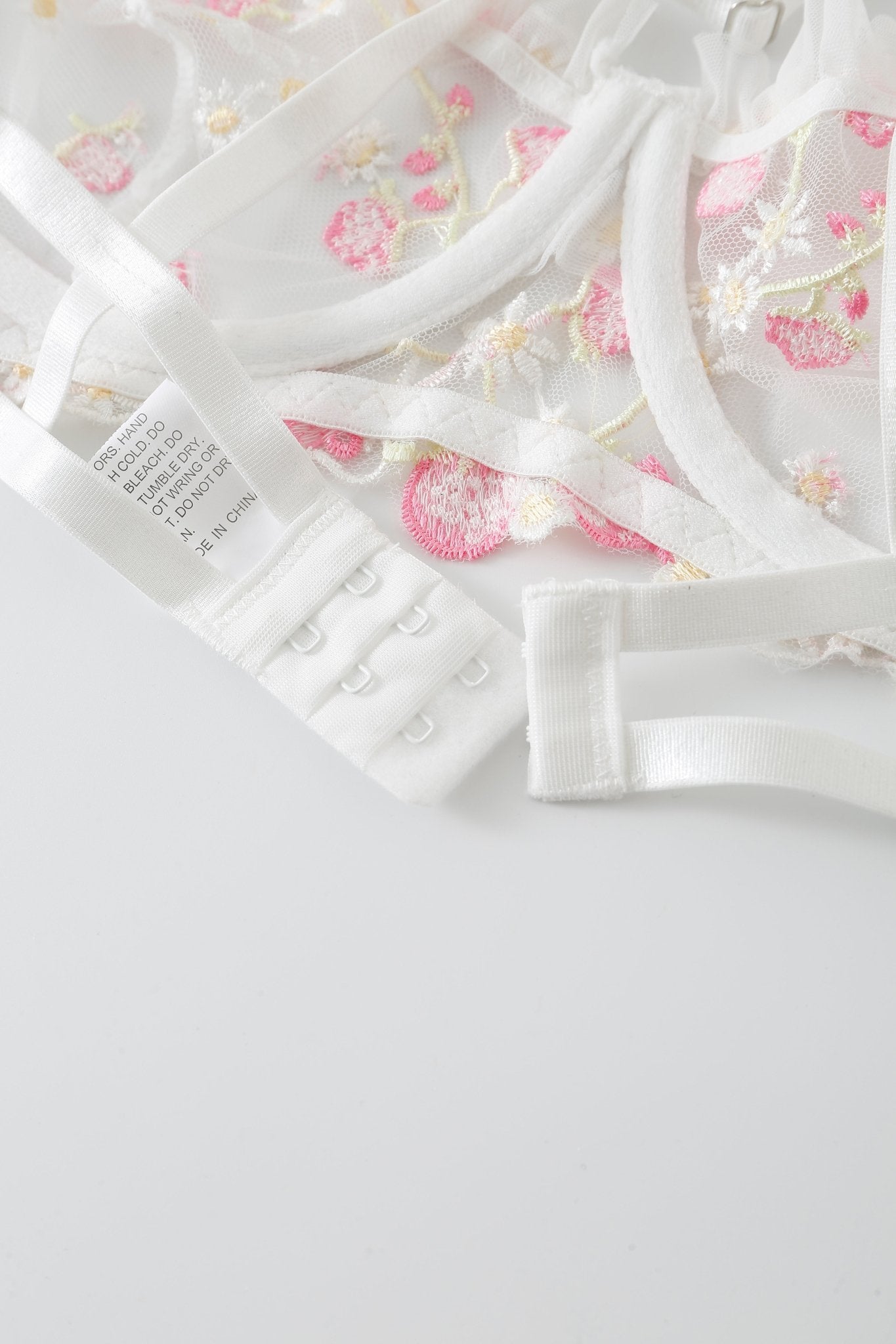 White bra from the Rosette w Pashmina - Full Set, featuring pink and yellow floral embroidery, displayed flat to show the hook-and-eye closure and fabric care tag—a sophisticated piece from the Rosette lingerie collection.